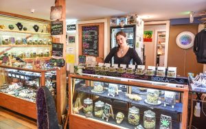 Kolbe Rose, the manager of Stoney Moose cannabis store, stands behind some of the stores display cases Wednesday, March 6, 2019, in Ketchikan, Alaska. Alaska has moved closer to becoming the first in the country with statewide rules allowing onsite use of marijuana at specially authorized stores. Eric Riemer is a co-owner of The Stoney Moose retail marijuana shop in Ketchikan, a community that is a summer tourist destination in southeast Alaska. He said his business, which is not in a stand-alone building, has had to revise its initial vision of an upstairs consumption area as the regulations took shape and is now looking at some type of outdoor area. (Hall Anderson/Ketchikan Daily News via AP)