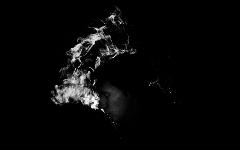 Smoke surrounds a woman's head in a dark setting