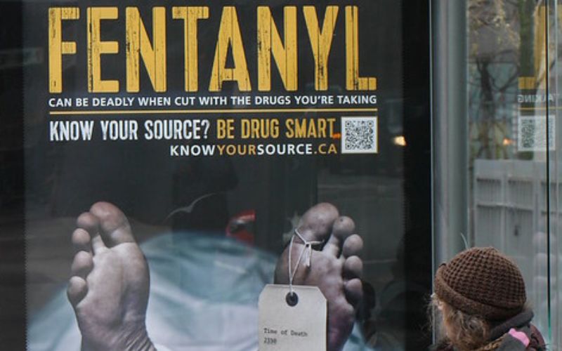 A woman looks at a bus stop PSA about fentanyl laced drugs