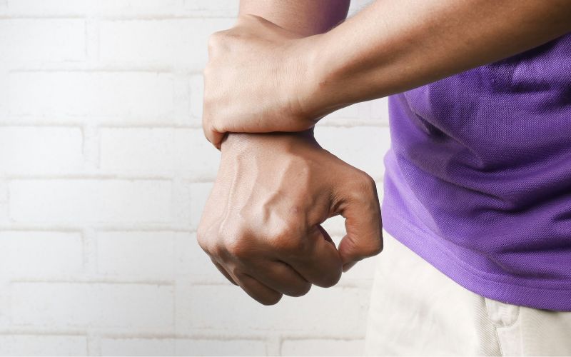 A man in a purple shirt holds their wrist in pain and balls their fist.