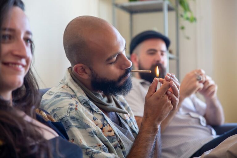 Two beareed men and one woman, early 30s, smoking cannabis joints inside on a couch.