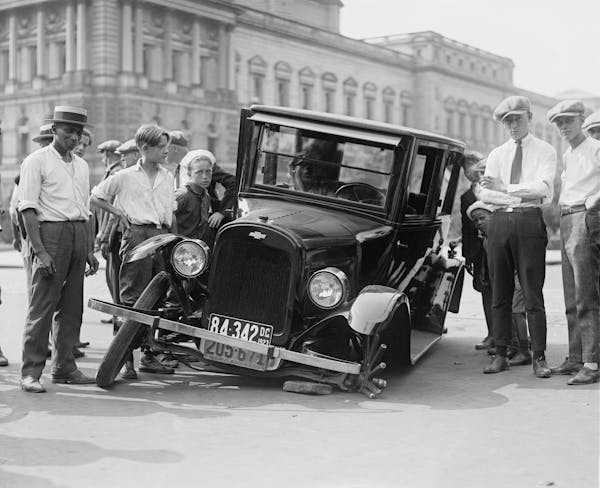 a tire has fallen off an old car with a group of people helping.