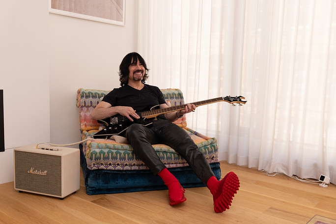 Josh Kesselman sits in a chair by an amplifier playing a guitar.